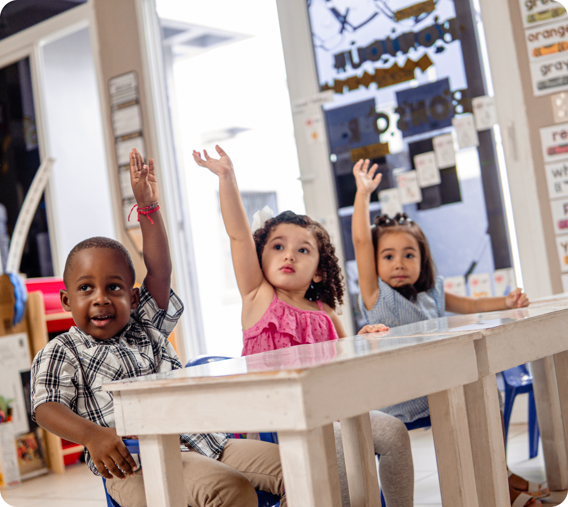 Three children raising hands in classroom.